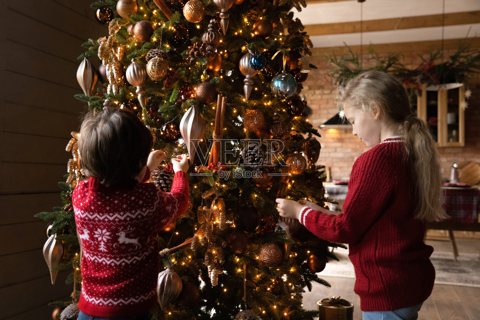 快乐的小朋友兄弟姐妹用装饰小玩意设计圣诞树。照片摄影图片