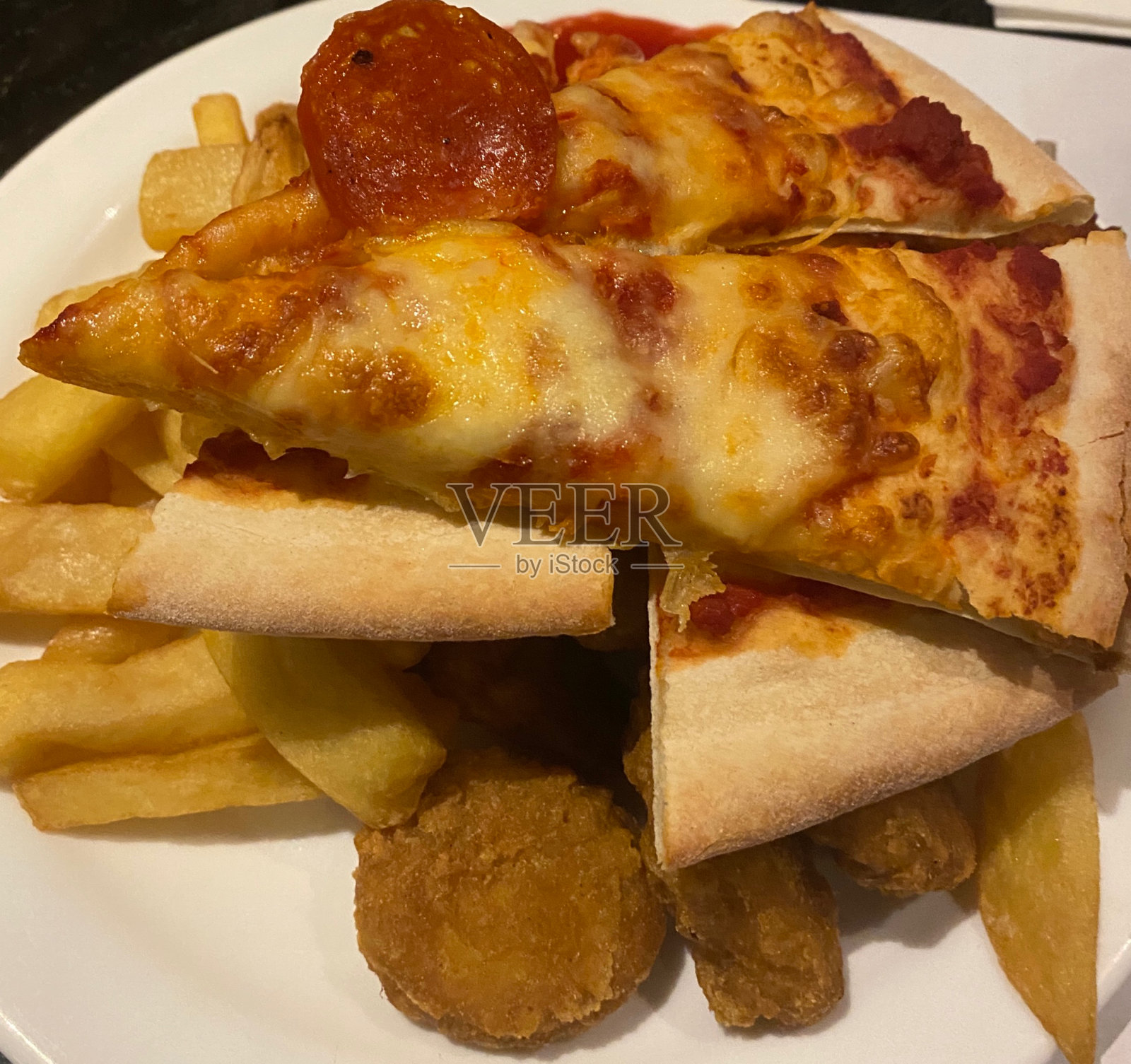 陶瓷盘子里塞满了鸡块和薯条的意大利辣香肠披萨照片摄影图片