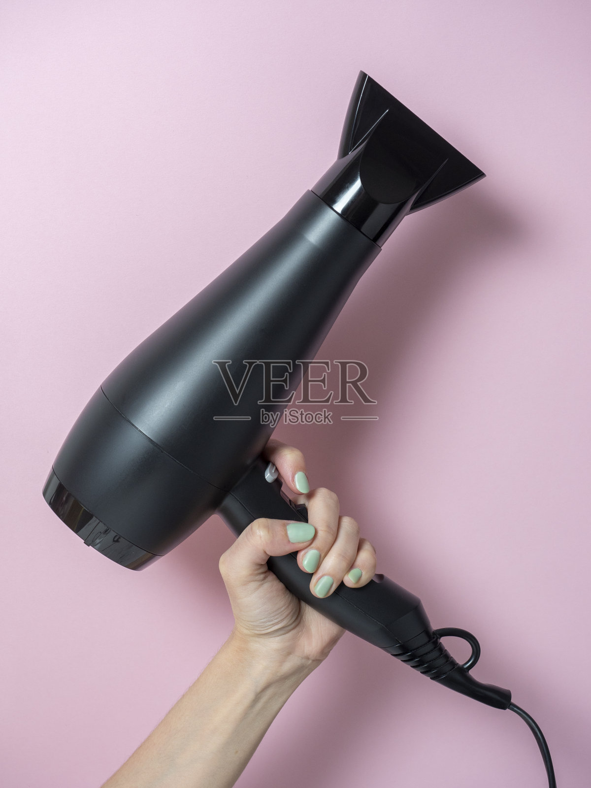 一个女人手里拿着黑色的吹风机，背景是粉红色的。头发护理产品。垂直图照片摄影图片