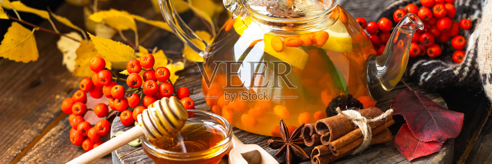 暖秋饮料的概念。热草药茶沙棘和香料:八角，肉桂，丁香，小豆蔻。温馨的家，香薰。木制背景，黄色落叶作为装饰。横幅照片摄影图片