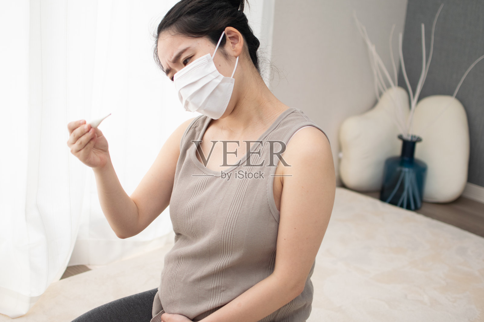 一位年轻的亚洲孕妇戴着口罩检查体温计照片摄影图片