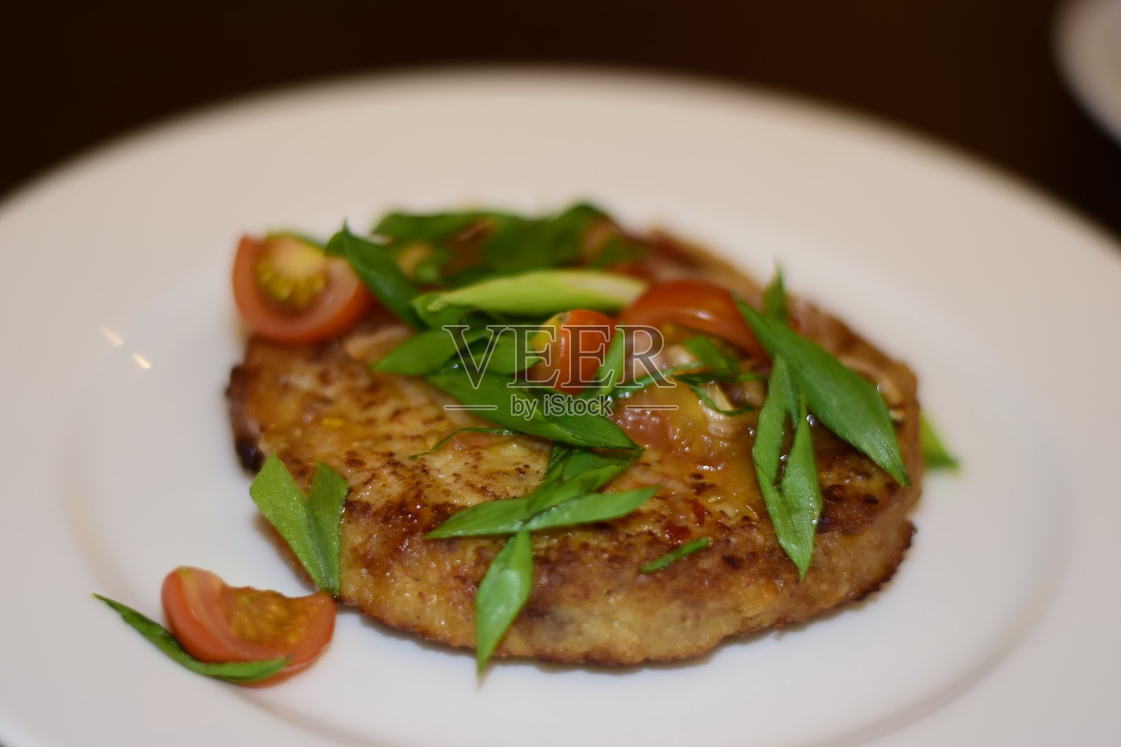 白盘子上有韭葱和圣女果的火鸡牛排照片摄影图片