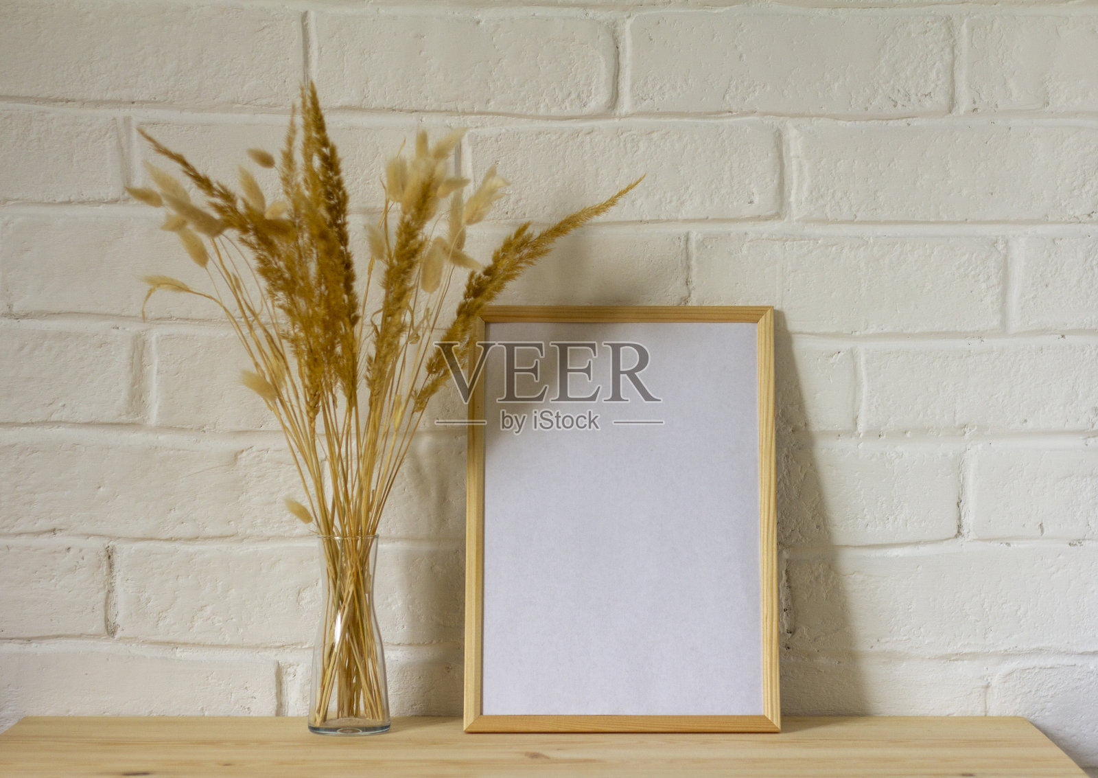 一个空相框的模型，木桌上透明的花瓶里放着一束秋天的干香草，还有一个空间的复制品。照片摄影图片