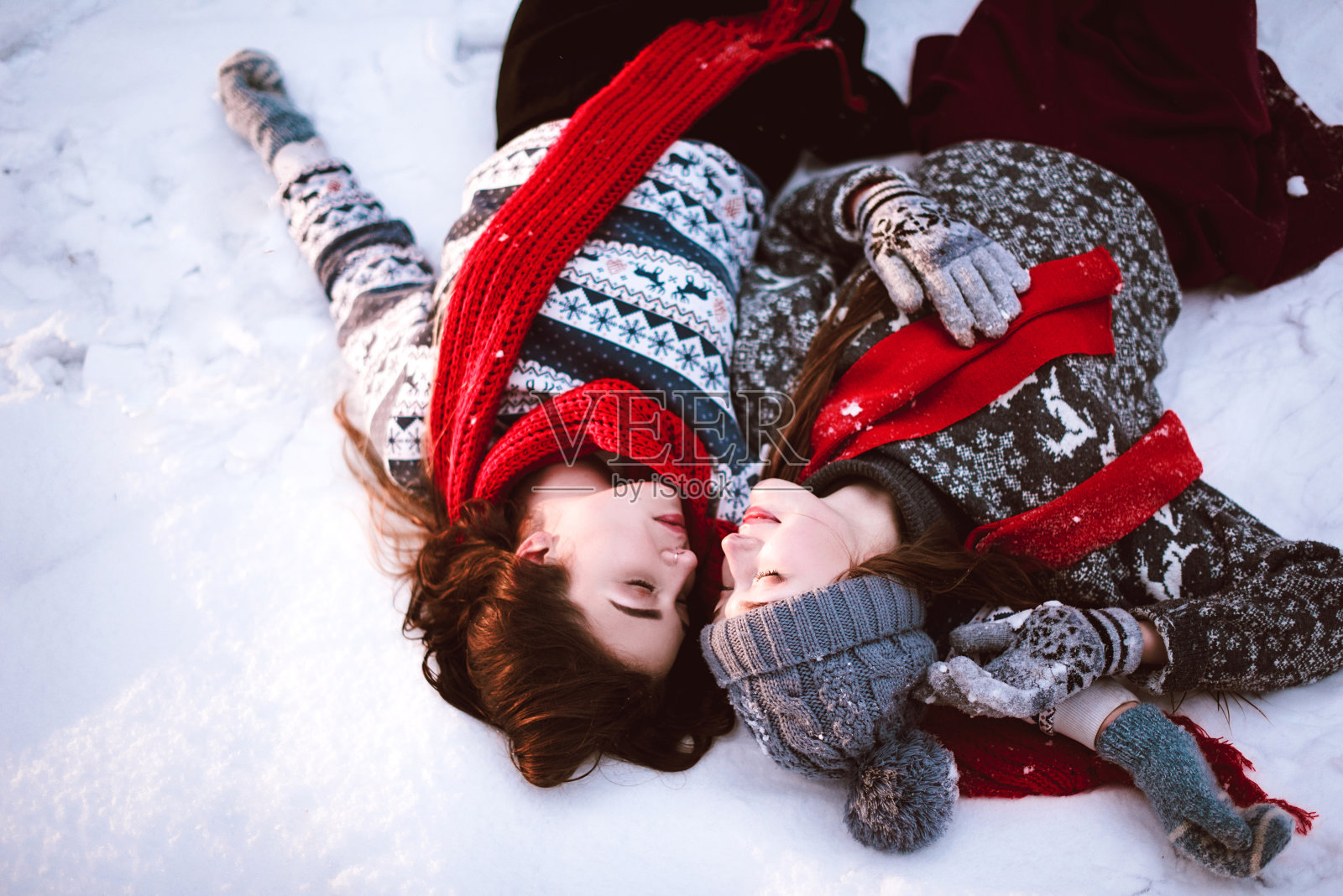 两个年轻的潮女朋友在一起。近距离时尚肖像两姐妹拥抱和乐趣躺在冬季森林的雪，穿着毛衣和围巾，最好的朋友夫妇户外，下雪的天气照片摄影图片