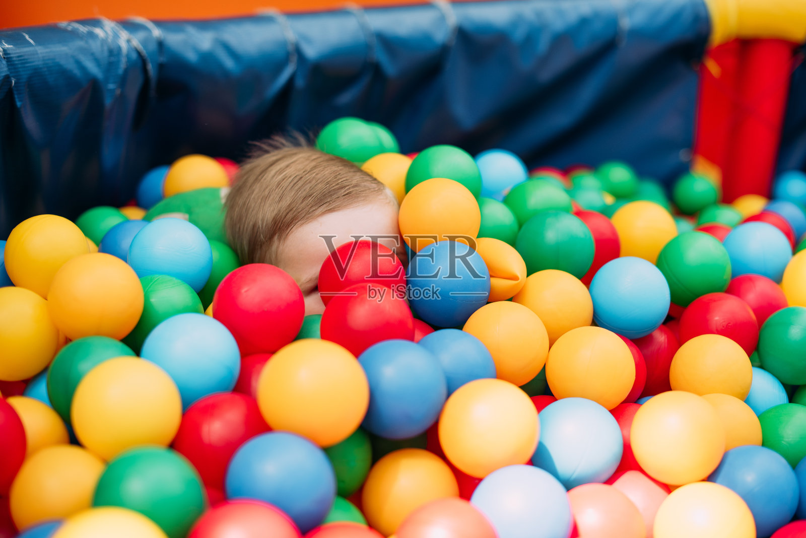 1-2岁男孩在儿童游乐场和室内游戏中心举办的生日派对上，在球坑里开心地笑。孩子们在操场的球池里玩着五颜六色的球。给小孩子的活动玩具照片摄影图片