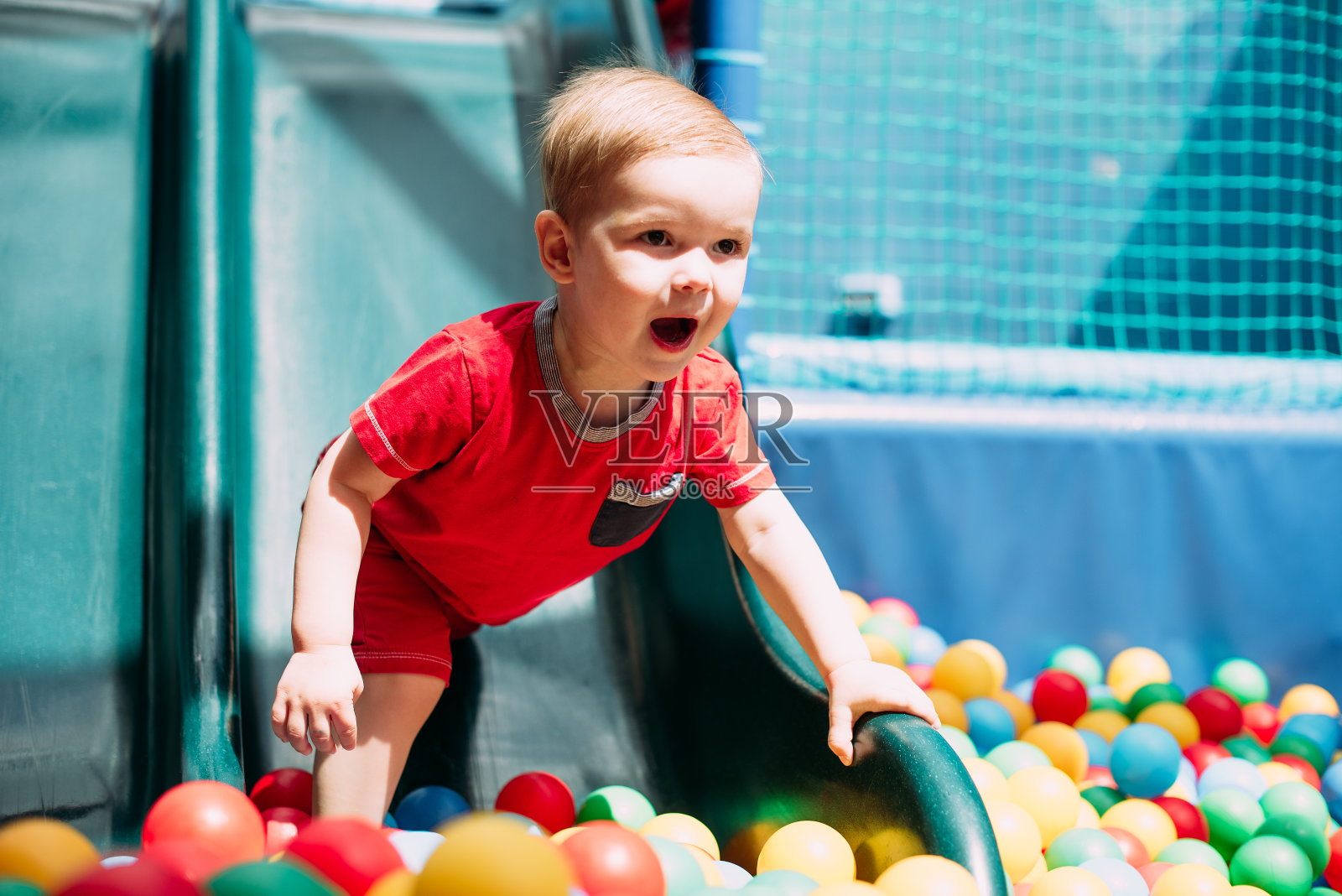 1-2岁男孩在儿童游乐场和室内游戏中心举办的生日派对上，在球坑里开心地笑。孩子们在操场的球池里玩着五颜六色的球。给小孩子的活动玩具照片摄影图片