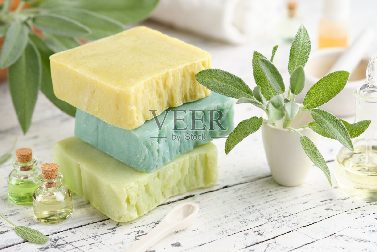 自制天然有机皂条，瓶装精油和新鲜的绿色鼠尾草叶放在白色的桌子上。照片摄影图片