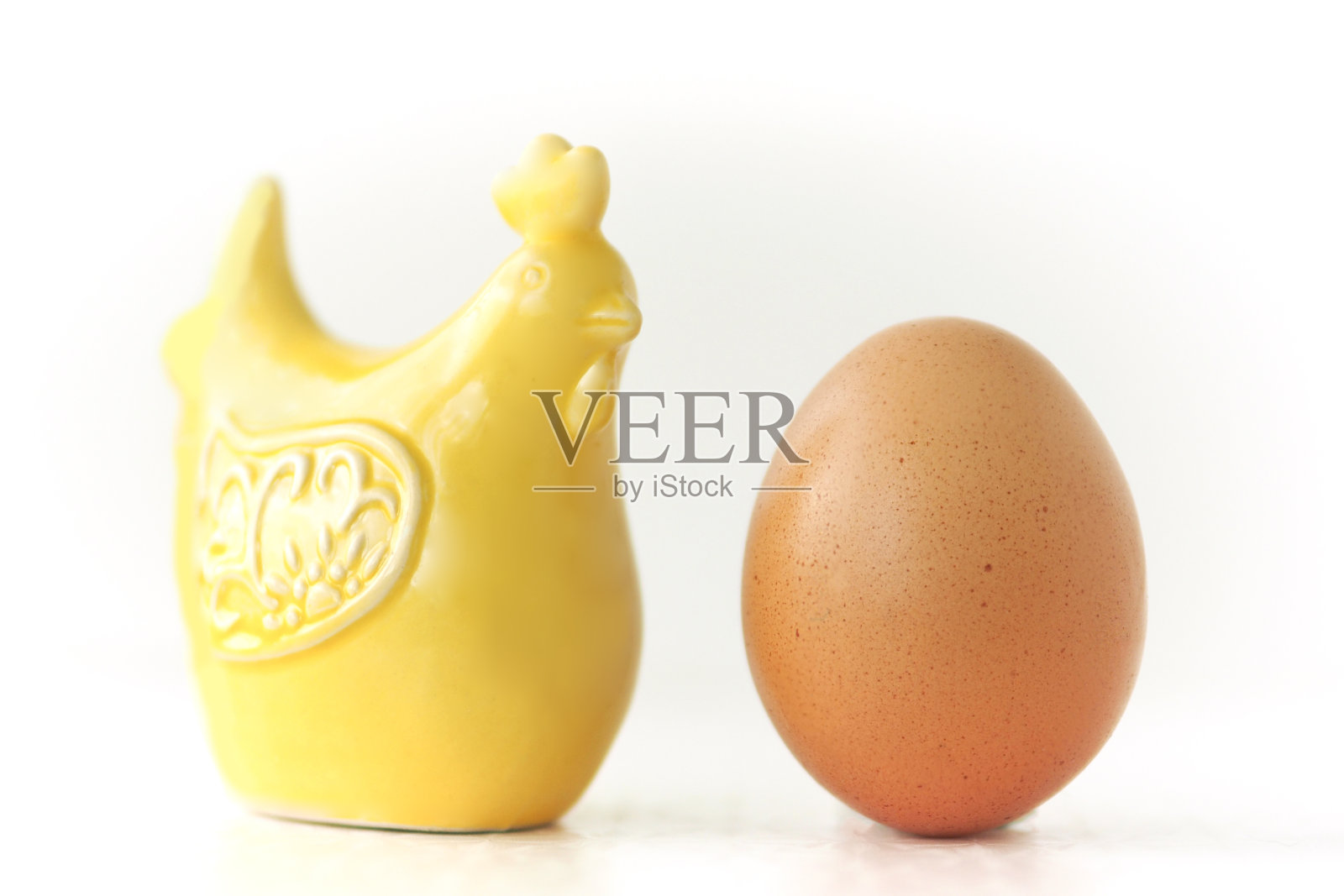 一只鸡和一个棕色的鸡蛋的黄色陶瓷雕像。在白色背景上隔离。照片摄影图片