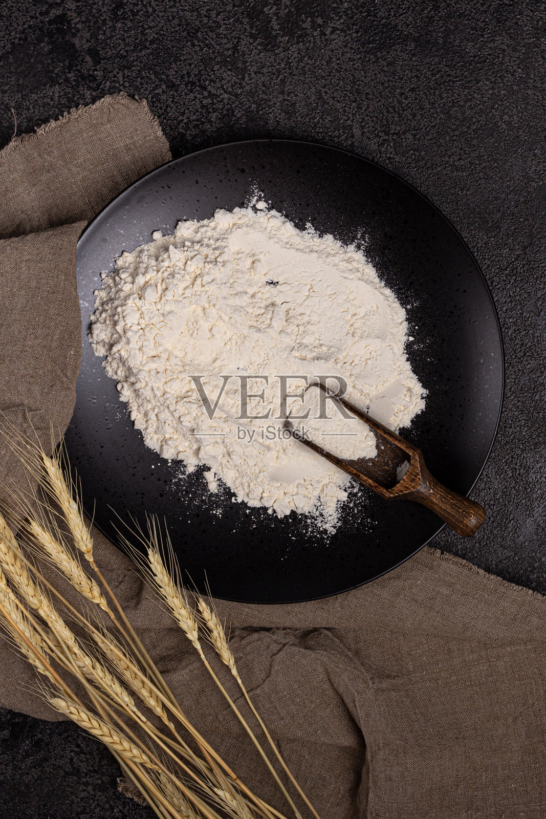 用面粉勺把面粉盛在盘子里。黑色背景的纹理。耳朵的小麦照片摄影图片
