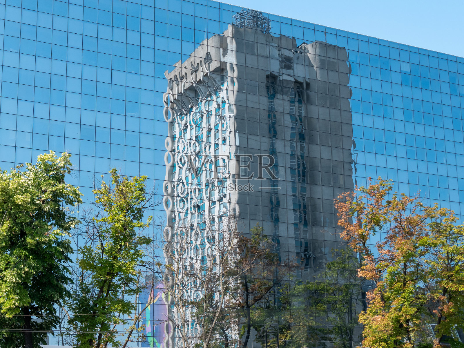 在现代办公大楼的玻璃幕墙上，映衬着一片蓝天和一座高大的现代建筑。照片摄影图片