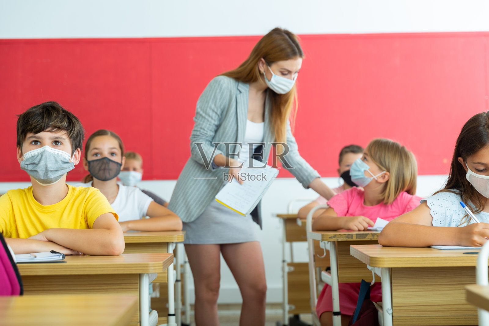 小学男生和女生戴着口罩听老师讲课照片摄影图片