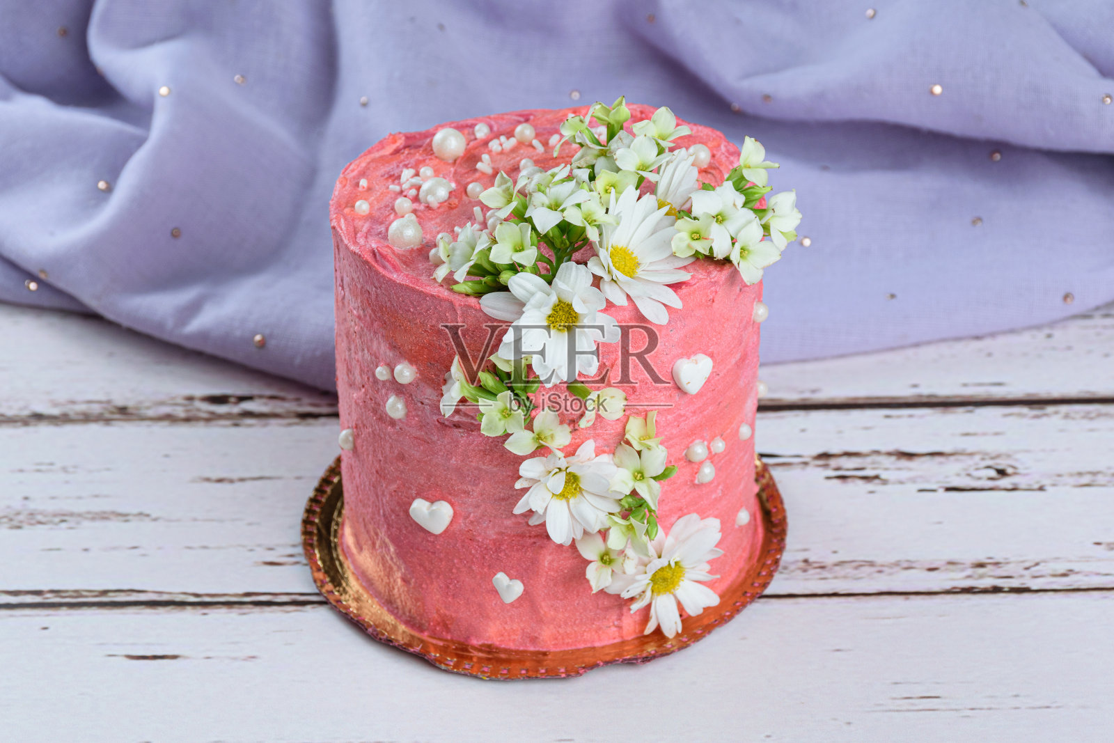 巧克力蛋糕上覆盖着粉红色的白脱奶油。用白色的心、珍珠和花朵装饰。背景是淡紫色的织物。照片摄影图片