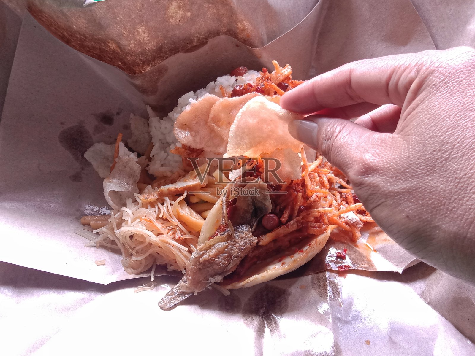 右手从米饭包里拿饼干，配菜有咸鱼、单面煎蛋和美味的面条照片摄影图片