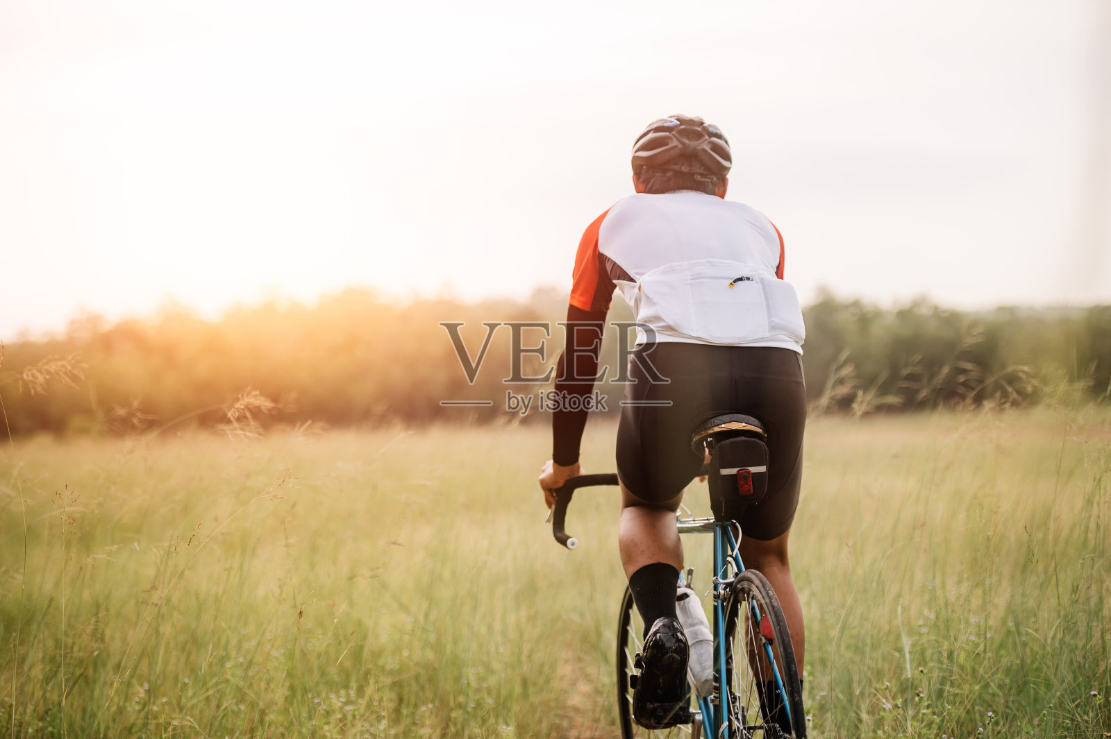 一个男人骑着自行车在路上。一名男子骑着老式运动自行车进行晚间锻炼。一个人骑着自行车在大自然、草地、森林中呼吸新鲜空气，傍晚的阳光透过照片摄影图片