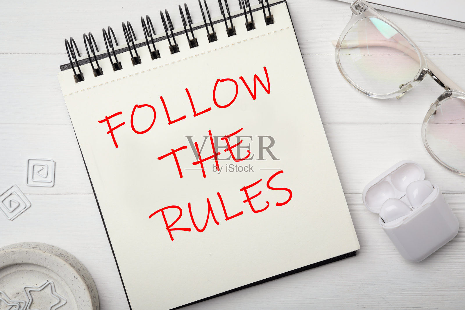 笔记本上的文字遵循规则，眼镜和耳机放在白色木桌上，平躺照片摄影图片