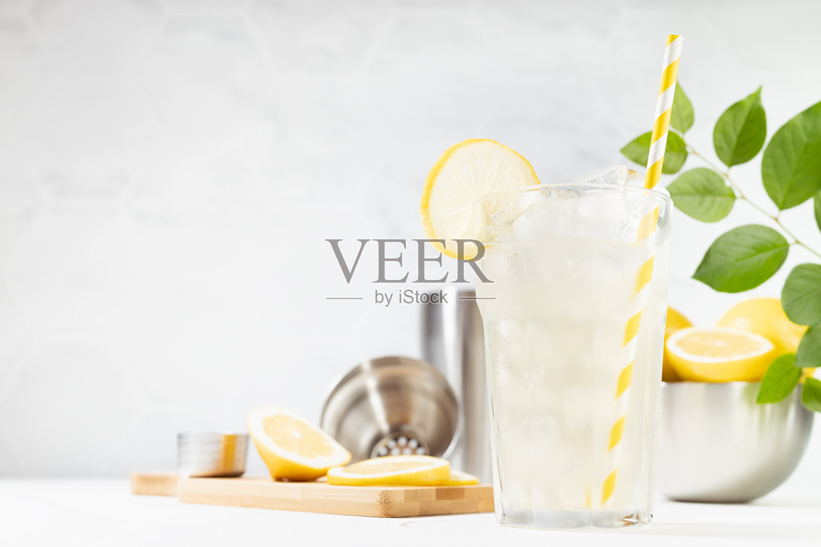 健康的维生素柠檬饮料在柔软的白色厨房与大理石瓷砖，在阳光下绿叶或户外-新鲜的天然柠檬水与冰，成分在白色木桌。照片摄影图片