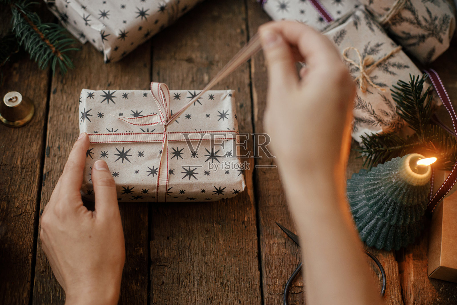 手打开时尚的圣诞礼物在质朴的木桌蜡烛，剪刀，冷杉树枝。圣诞快乐!时尚的斯堪的纳维亚圣诞礼物，大气的情绪化形象照片摄影图片