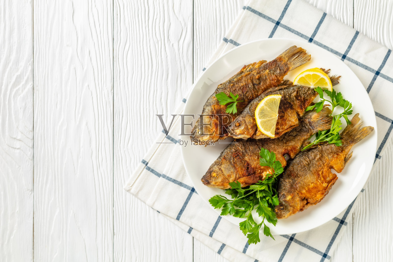 炸鲫鱼金黄酥脆的外皮放在白色的盘子里，配上香菜和柠檬放在白色的木桌上，平铺，空间自由照片摄影图片