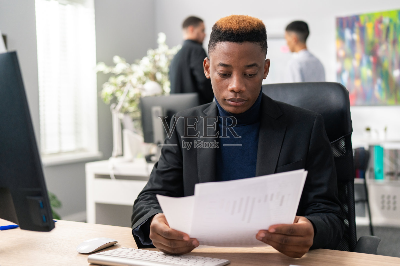 一个头发奇特的小男孩坐在公司办公桌前的椅子上，手里拿着报告、文件，仔细阅读、分析笔记，专注、专注、严肃，穿着夹克的员工照片摄影图片