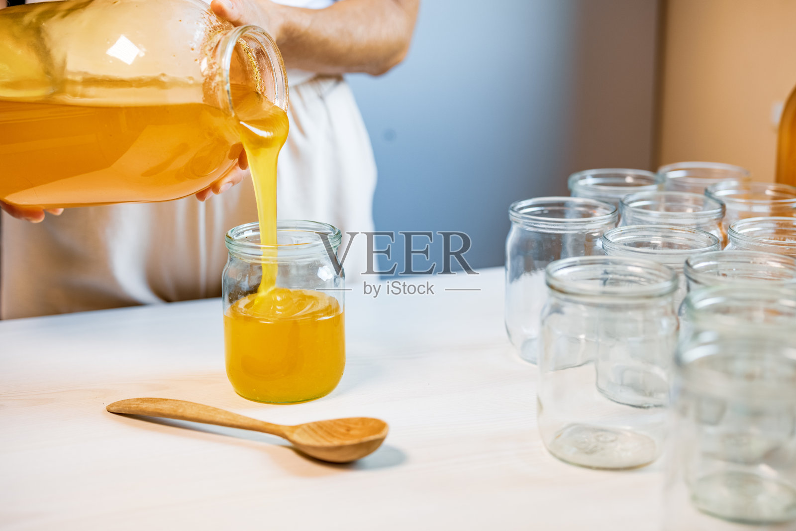 一个女人把蜂蜜倒进白色桌子上的透明罐子里照片摄影图片