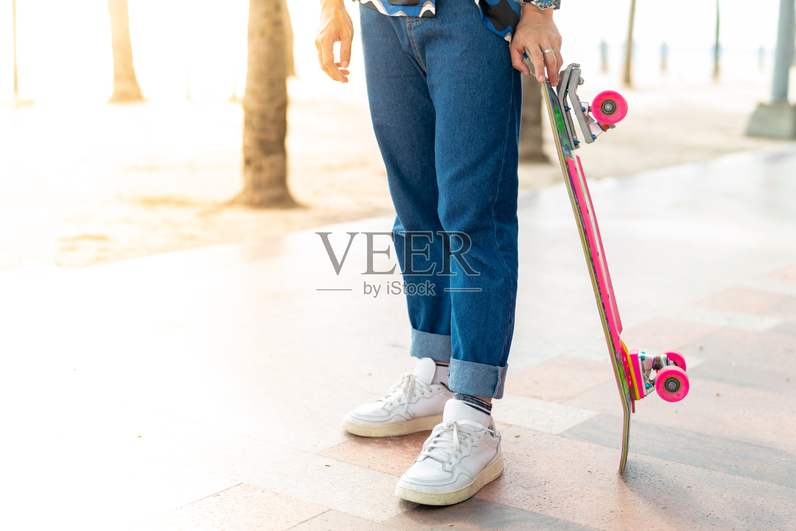 一个亚洲人的腿是站着的。手拿滑板站在方生海滩的人行道上。泰国照片摄影图片