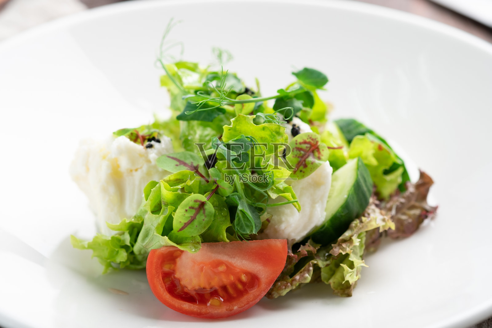 清淡的马苏里拉奶酪和新鲜蔬菜沙拉——黄瓜，西红柿，生菜，豌豆放在木制背景的白色盘子里照片摄影图片