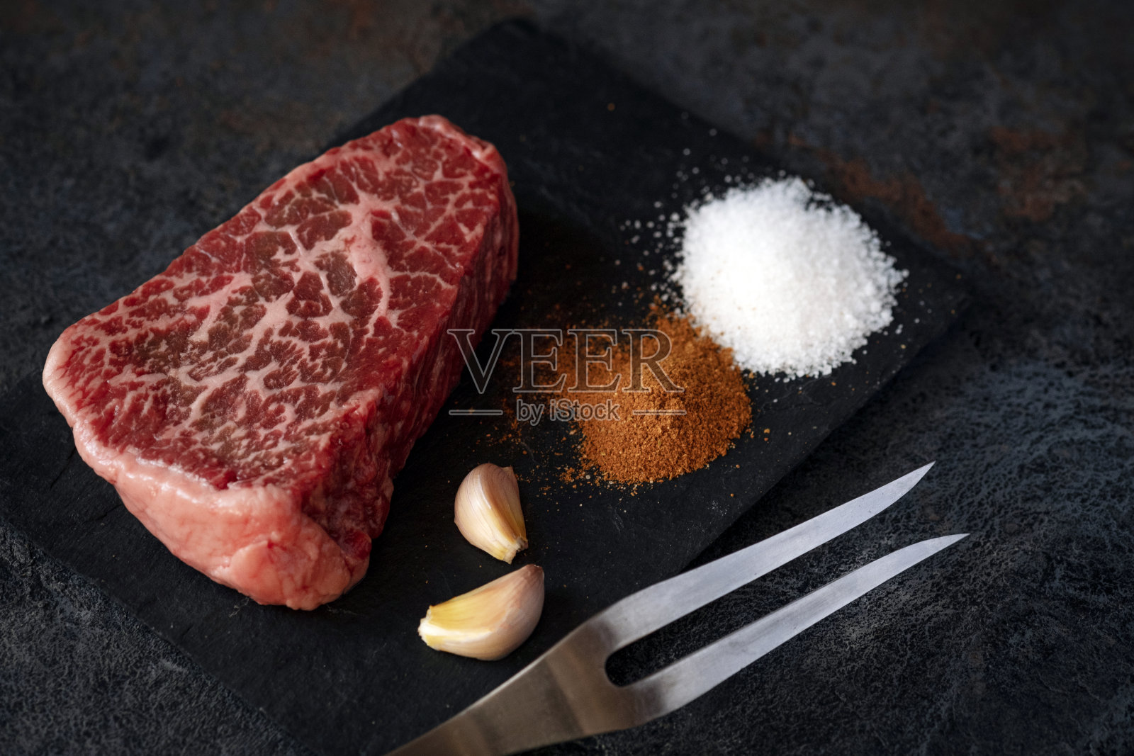 从牛颈上取下的生铁扒，黑色背景，加盐和调味料，供烧烤用照片摄影图片