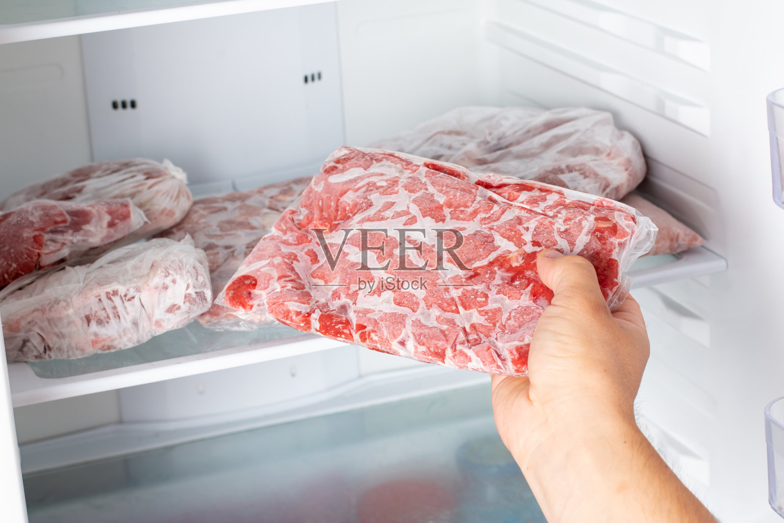 男人从家里厨房的冰箱里拿出一袋冻肉。照片摄影图片