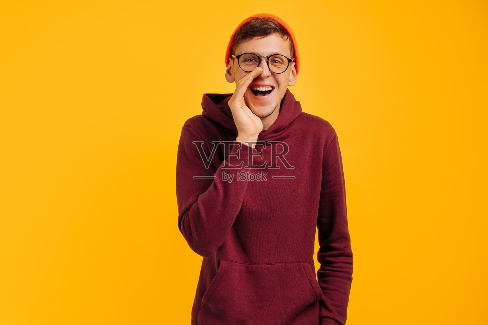 英俊的男人在秘密地说着什么，一个戴着橙色帽子和红色毛衣的男人在闲聊，穿着灰色衣服照片摄影图片