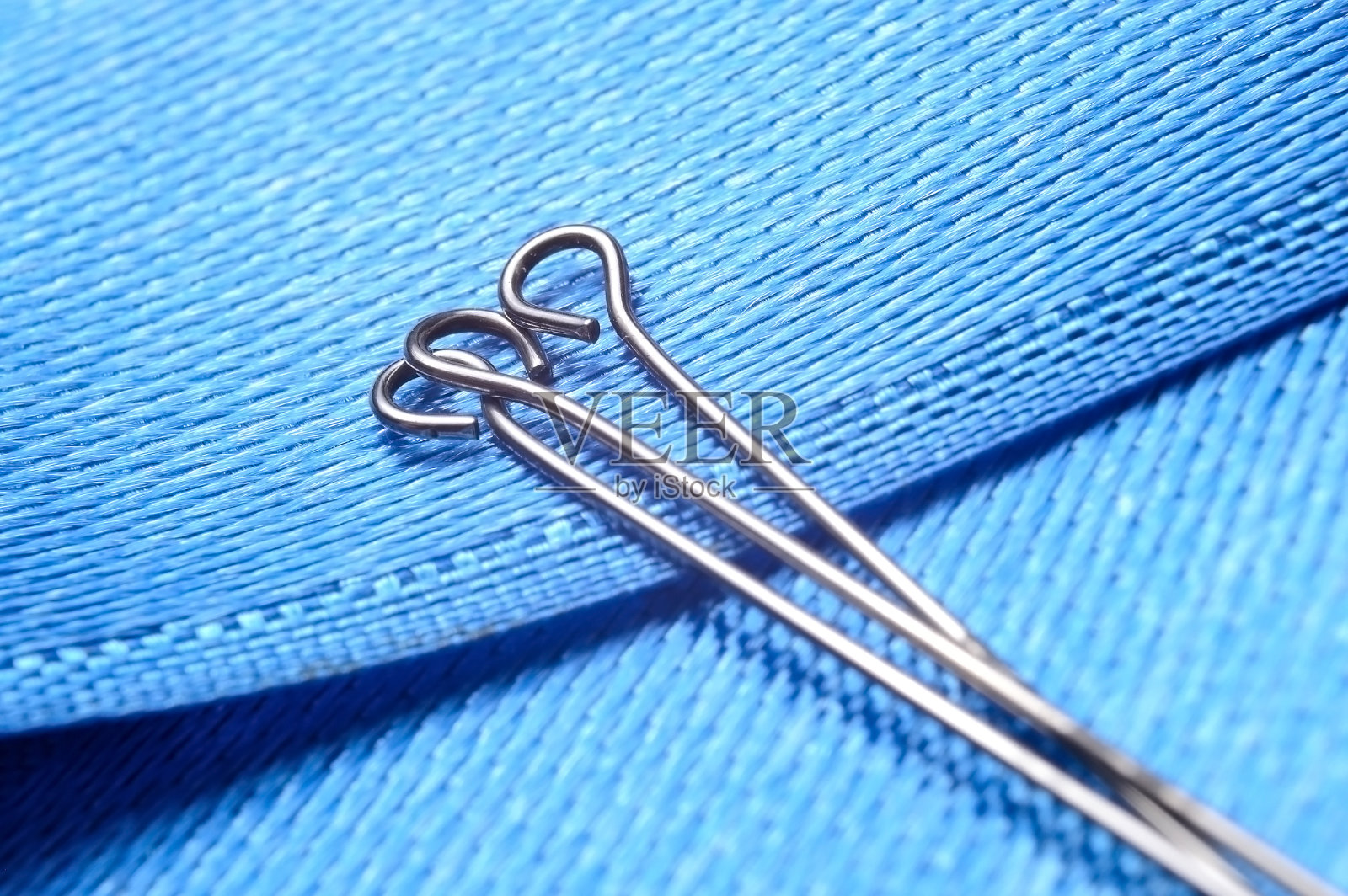 蓝色织物背景上有三个别针。特写镜头。照片摄影图片