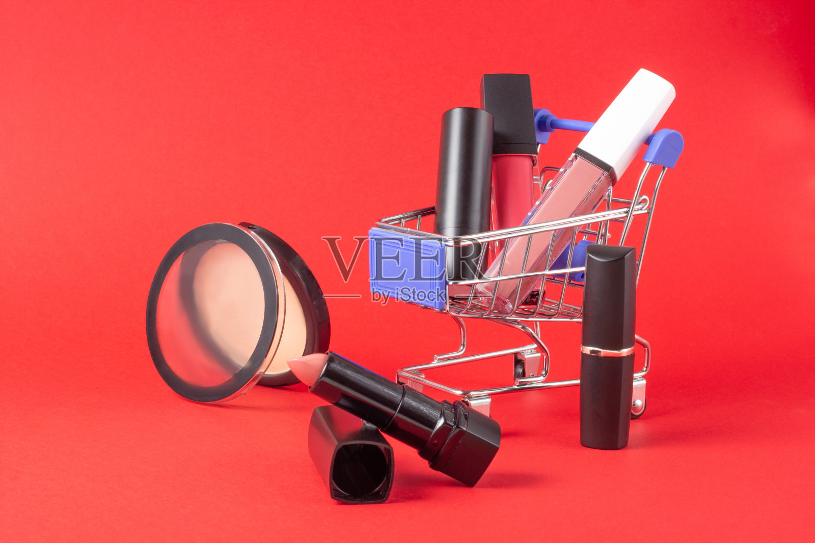 一套口红，化妆品和唇彩，粉，眼影和一个购物车在亮红色的背景。买化妆品的概念，网上购物，度假照片摄影图片