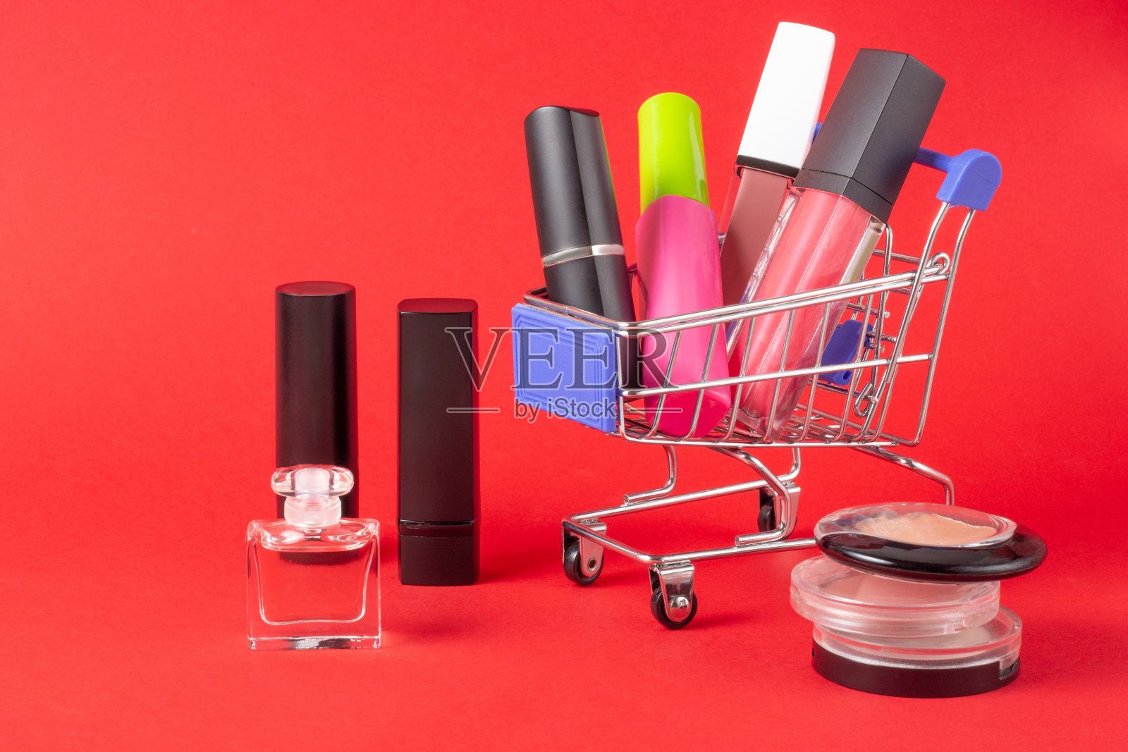 一套口红，化妆品和唇彩，粉，眼影和一个购物车在亮红色的背景。买化妆品的概念，网上购物，度假照片摄影图片