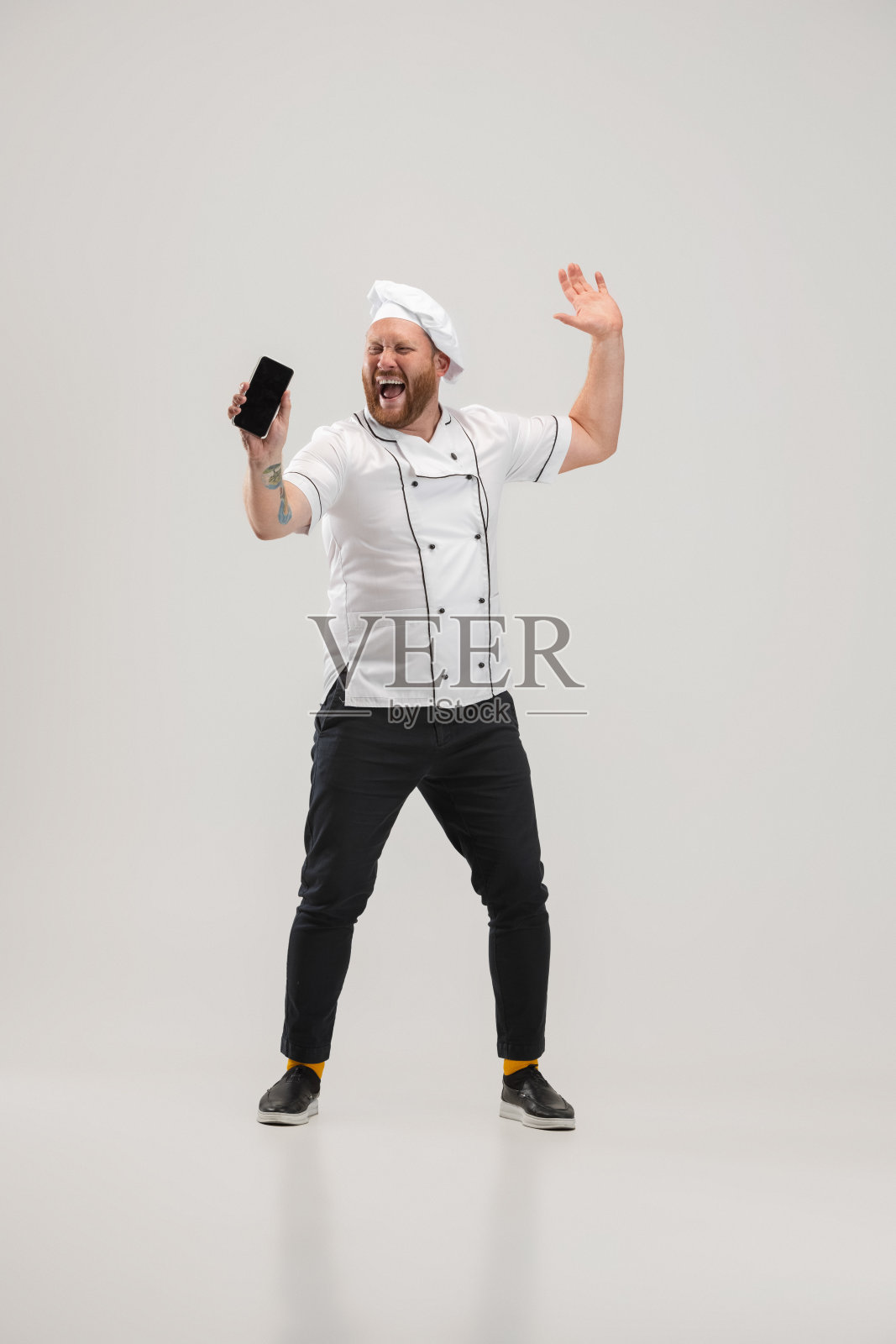 快乐厨师，厨师穿着制服用手机隔离在白色背景下。工作概念，职业，幽默，面部表情照片摄影图片