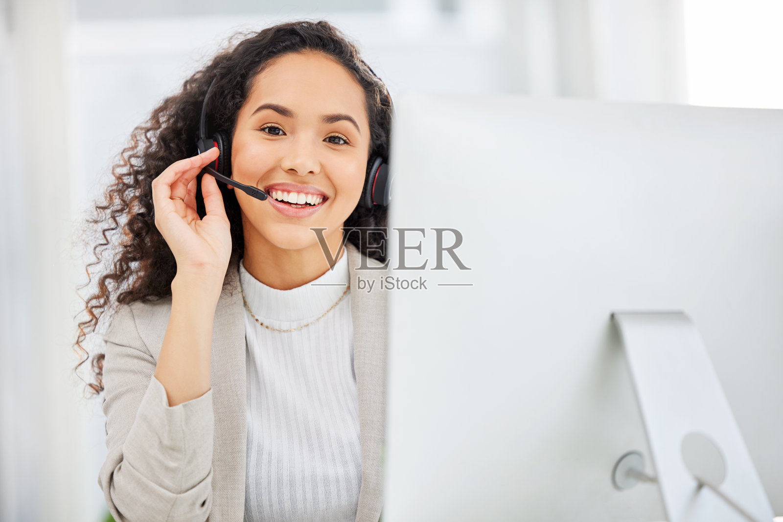 一名年轻的女商人戴着耳机在办公室的电脑前工作照片摄影图片