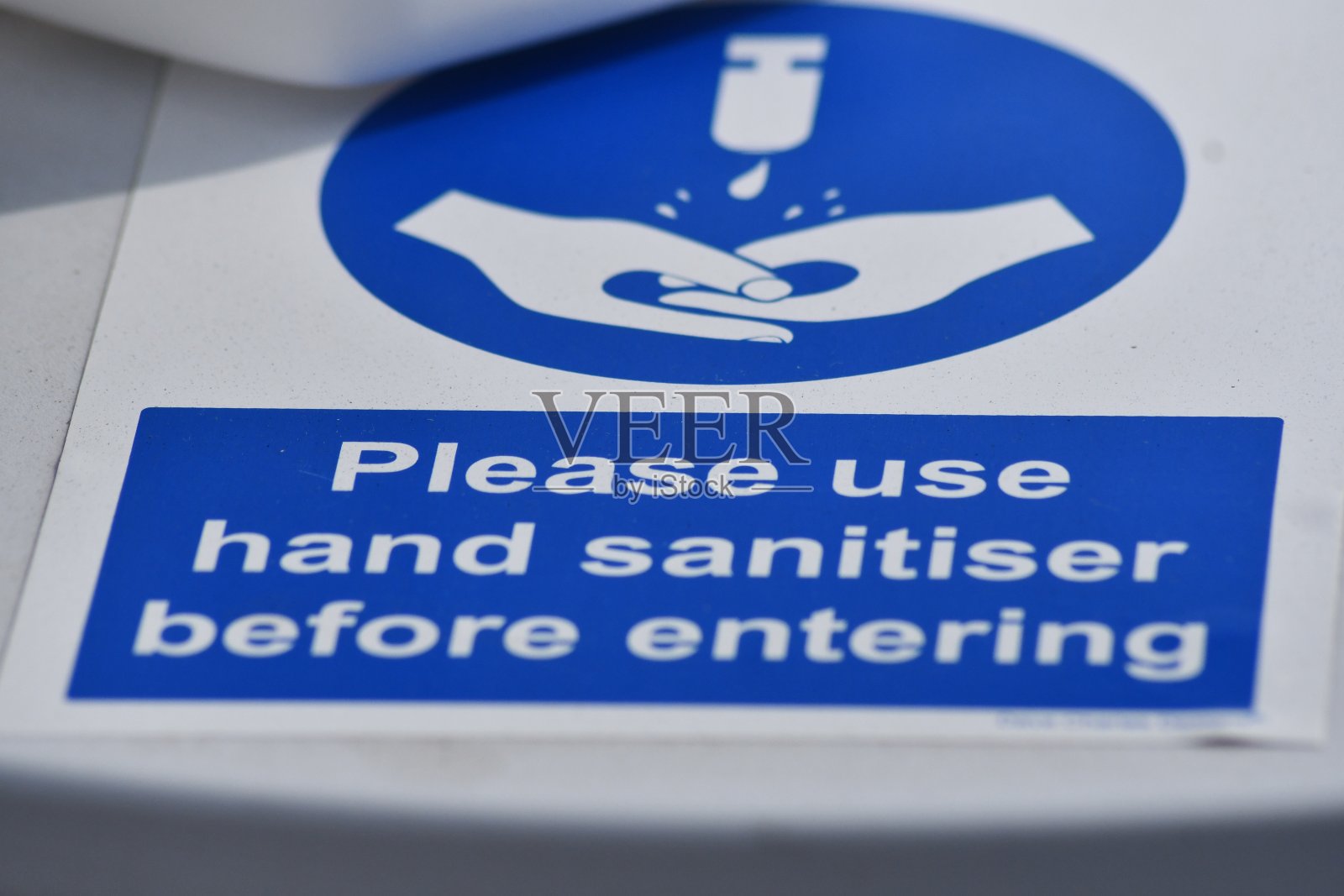 一个白色和蓝色的双手标志的角度视图，说明在冠状病毒大流行期间，进入前请使用洗手液照片摄影图片