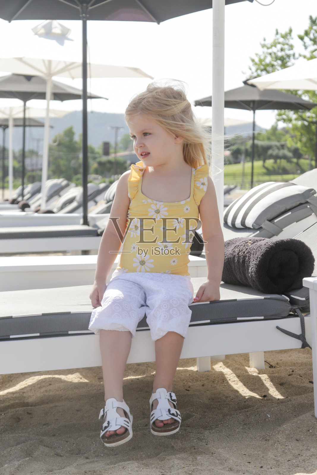 可爱的蹒跚学步的小女孩穿着黄色泳衣在海滩上享受一天。田园诗般的暑假。照片摄影图片