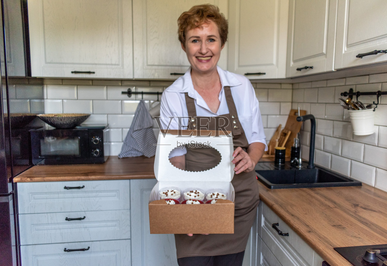 系着围裙的女人微笑着拿着一盒生日蛋糕。自制的生日甜点。照片摄影图片