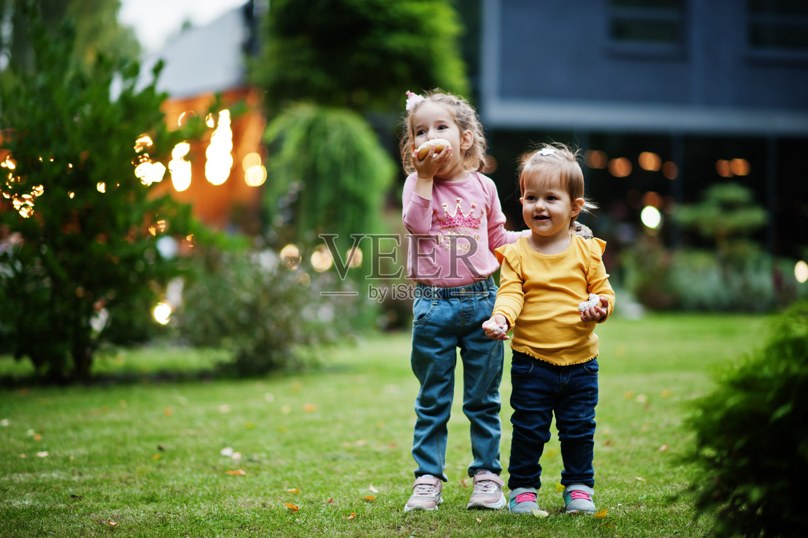 两姐妹在傍晚的院子里吃着甜甜圈。美味可口的甜甜圈食物。照片摄影图片