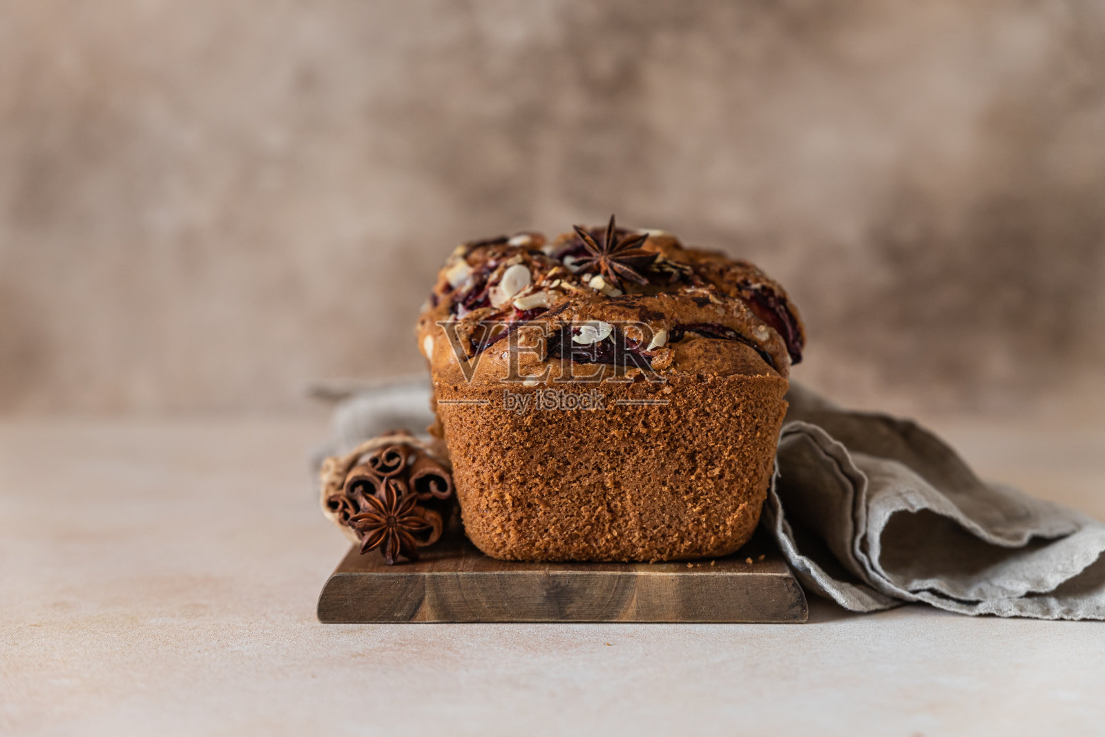 自制的香辣李子蛋糕，装饰有杏仁，木制的服务板，混凝土背景。葡萄干、香料和杏仁的面包蛋糕。照片摄影图片