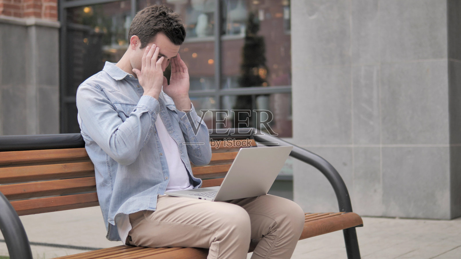 坐在户外用笔记本电脑头痛的年轻人照片摄影图片