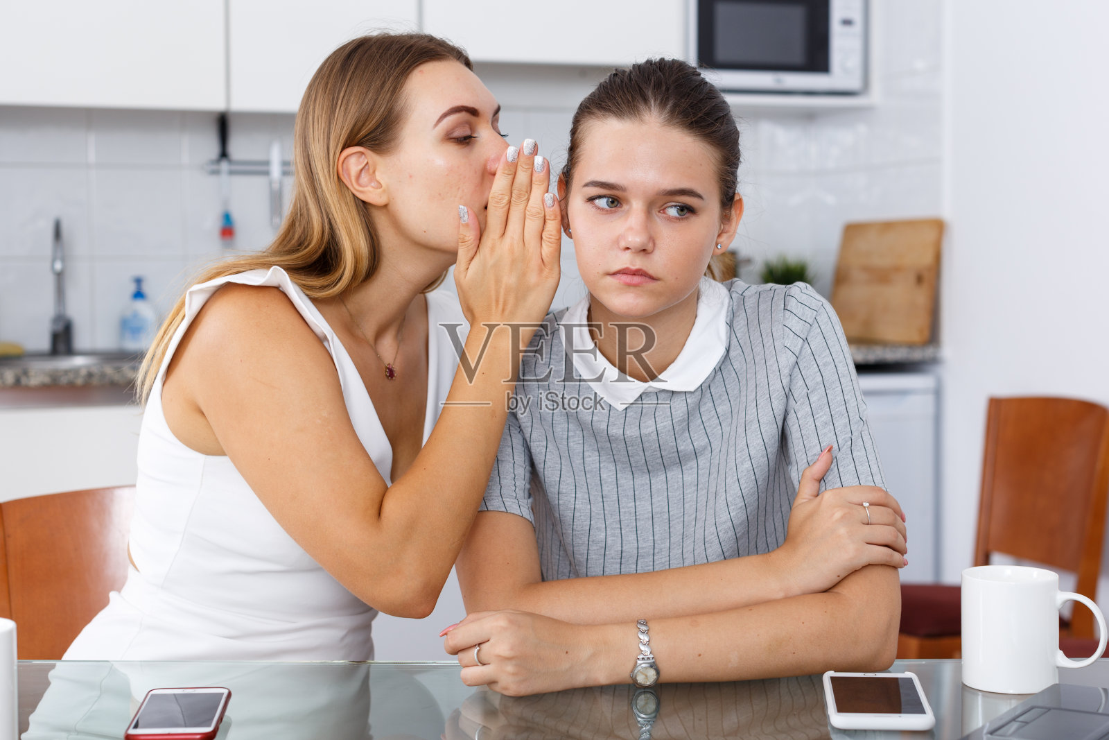 悲伤的年轻微笑的女友在耳边窃窃私语，分享秘密照片摄影图片