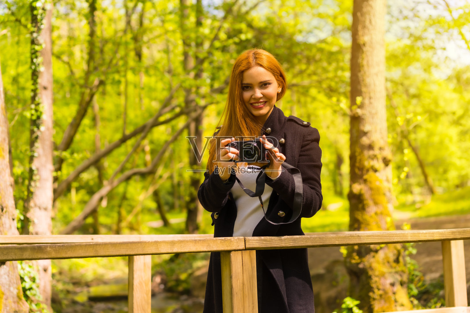 身穿黑色夹克的女摄影师在秋天的公园里，微笑着享受着日落时的拍照照片摄影图片