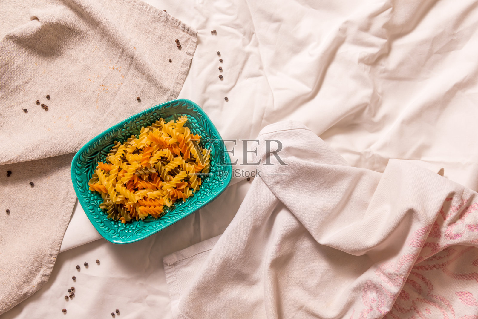 背景是有褶皱的浅色织物，蓝绿色的盘子和彩色的意大利面。照片摄影图片