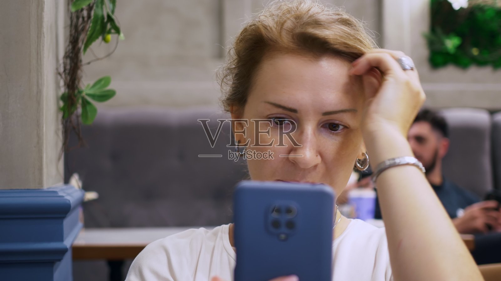 一名金发女子用智能手机摄像头当镜子拉直头发。一个女人坐在咖啡馆里等着和一个男人见面照片摄影图片