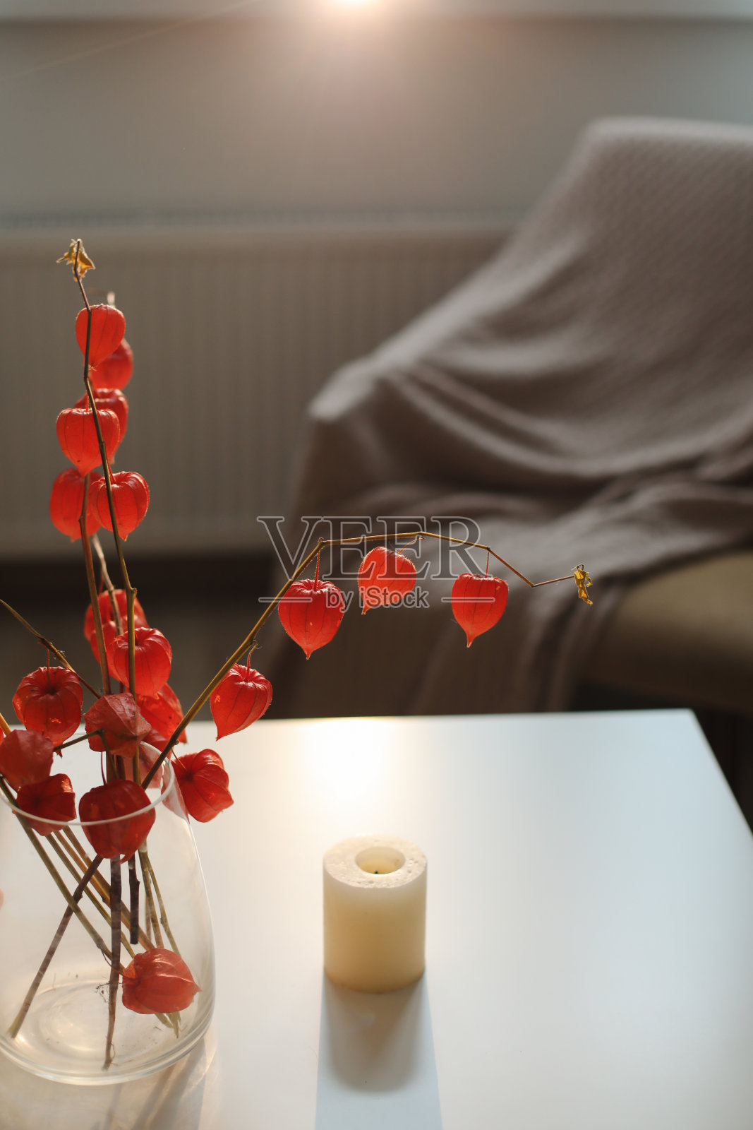 舒适的秋天静物、蜡烛、鲜花、花瓶里的橙色酸浆树枝和家庭内部的细节照片摄影图片