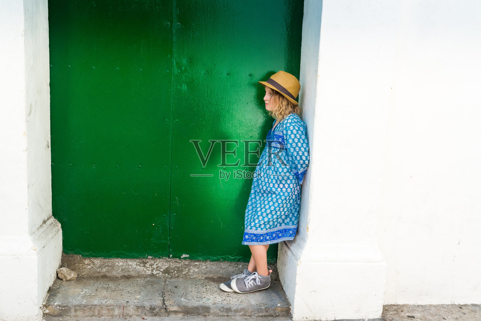 一个可爱的年轻女孩戴着软呢帽站在门口，古怪的肖像照片摄影图片