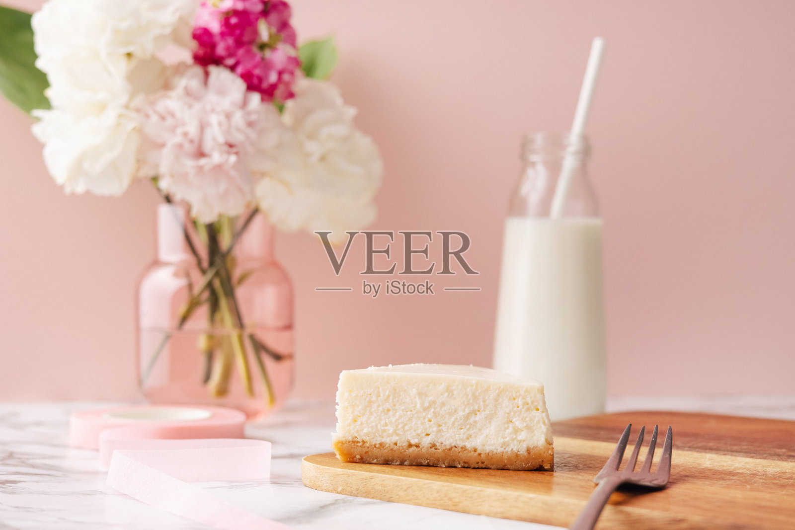 自制芝士蛋糕和牛奶。粉色背景的大理石桌上放着法式甜点和鲜花照片摄影图片