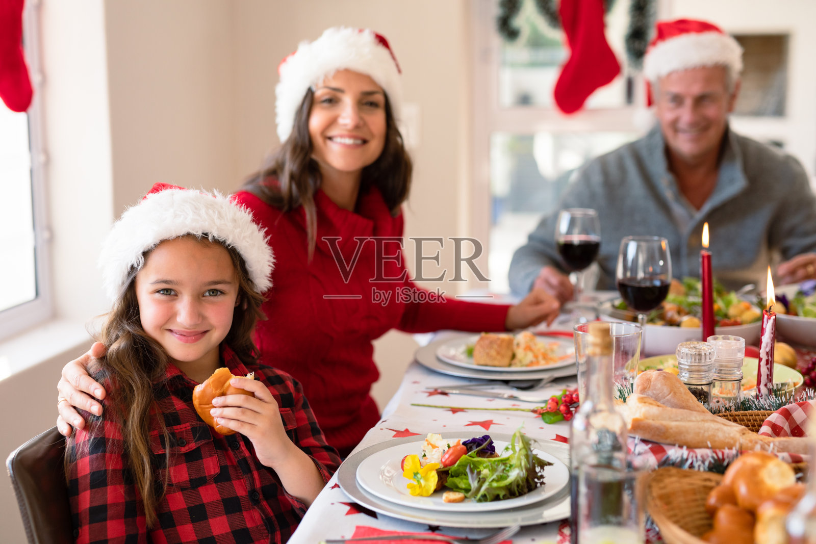 快乐的白种母亲和女儿戴着圣诞帽在圣诞节看着相机照片摄影图片