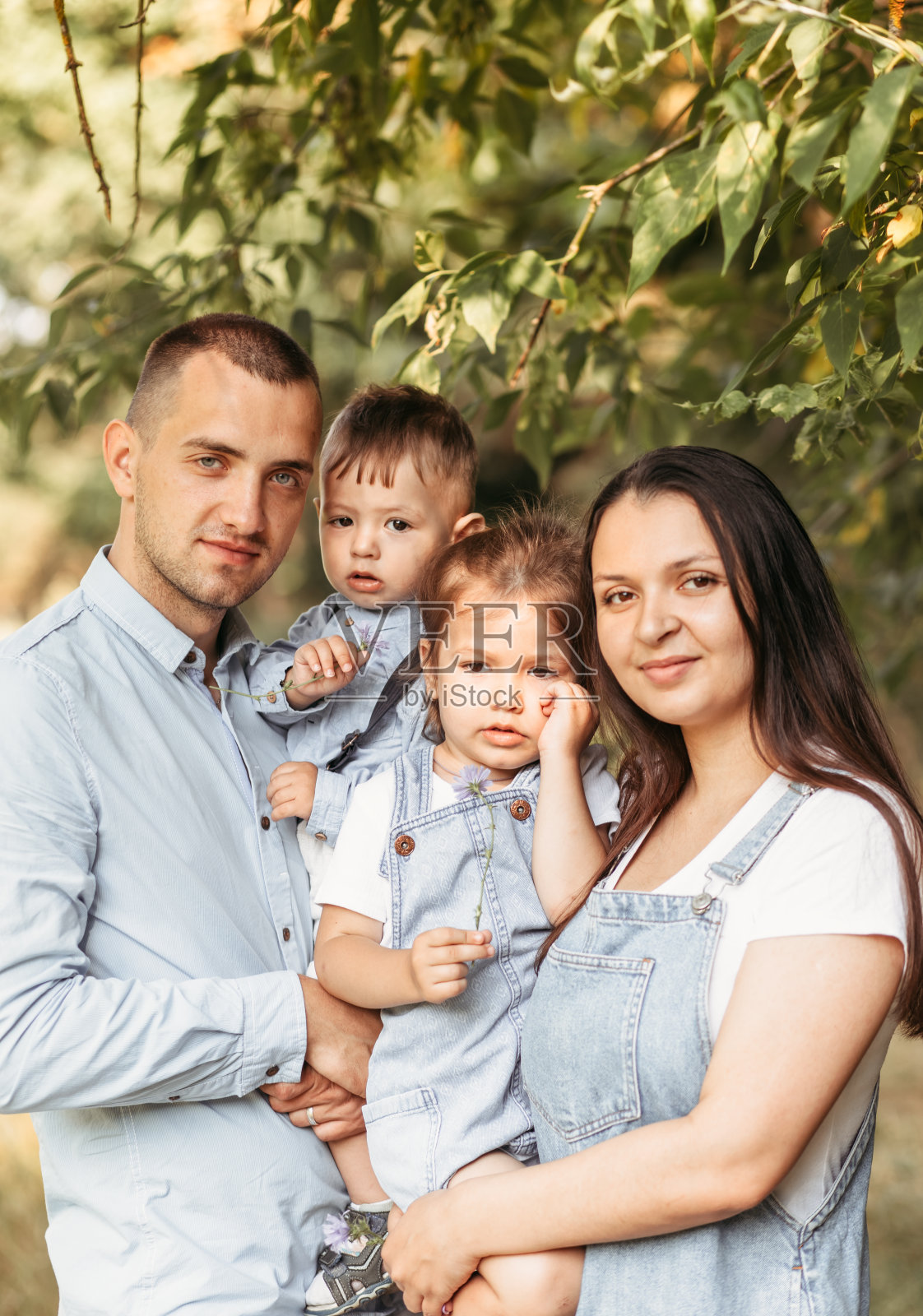 年轻幸福的一家人带着两个孩子在大自然的夏日里散步。健康微笑的爸爸，妈妈和孩子在一起照片摄影图片
