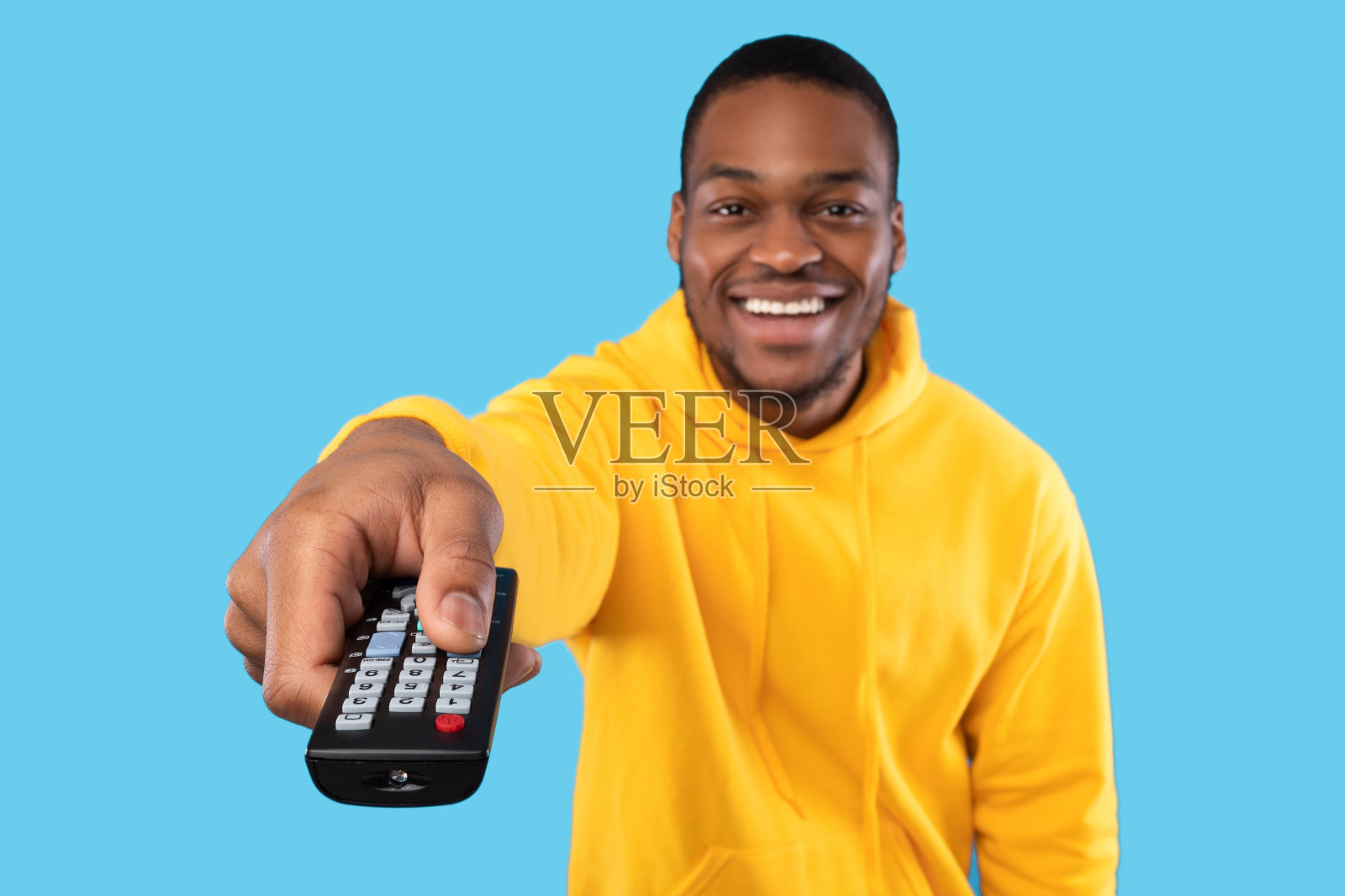 欢快的黑人看电视，指着遥控器，蓝色背景照片摄影图片